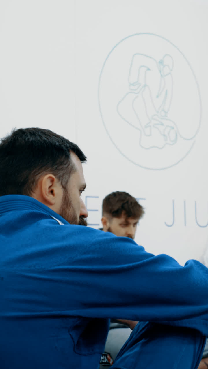 Member in a blue gi watching a demonstration, with the Concept Jiu-Jitsu logo behind